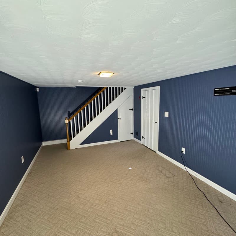 Basement painted with navy blue beadboard walls and white staircase in Lynnfield, MA